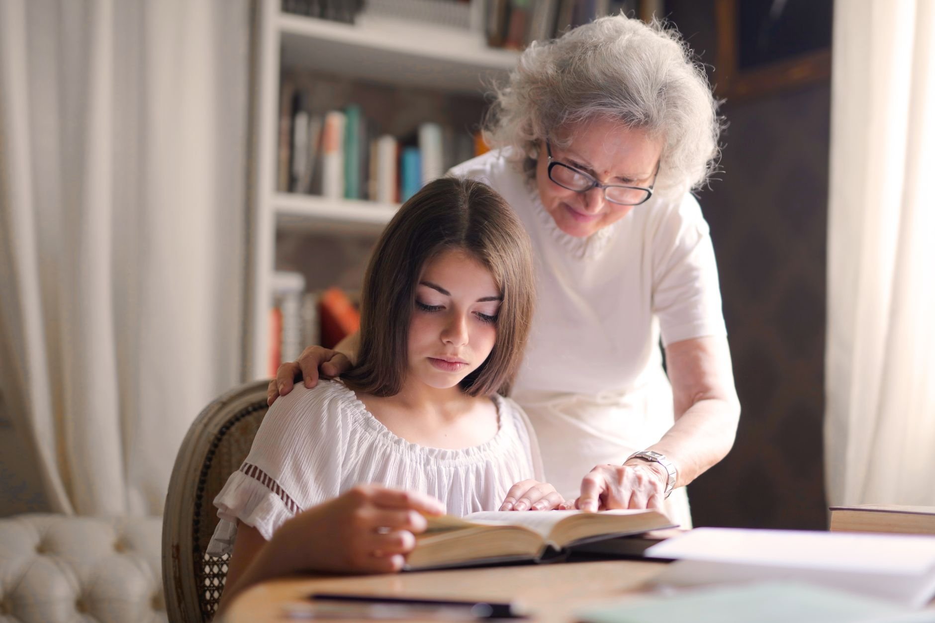 A grandmother and young girl reading a book together in a cosy indoor setting, fostering education and bonding.
